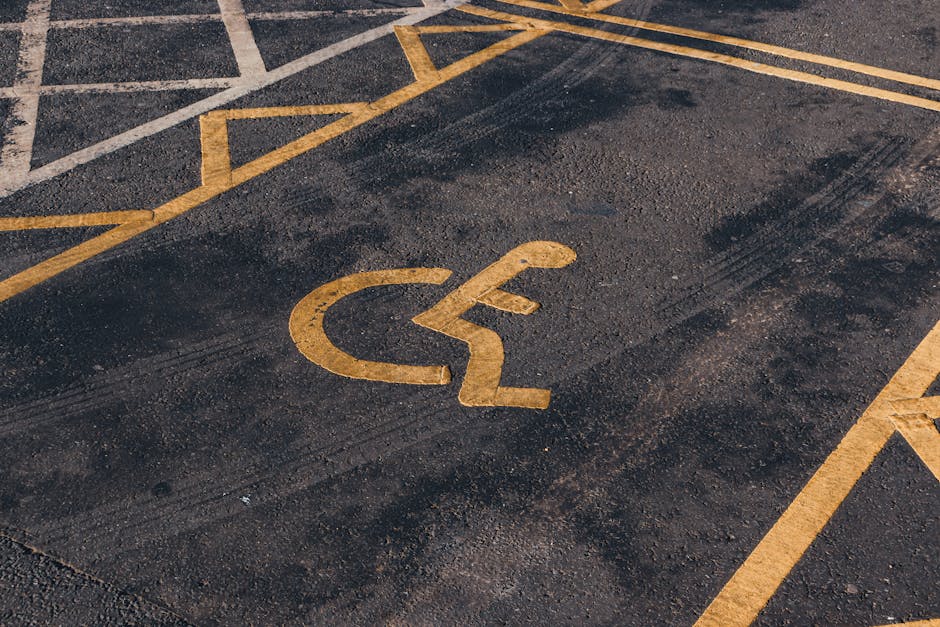 A blue and white parking sign indicating a designated disabled parking space is mounted on a metal pole against a dark grey wall. The sign features a large white letter 'P' with a blue background and includes a wheelchair symbol beneath it to specify accessibility. In the context of house removal services by Man with Van Stroud Green, this image relates to parking arrangements and access considerations during furniture transport and home relocation, highlighting the importance of identifying accessible parking spots for timely and efficient loading and unloading of moving vehicles.